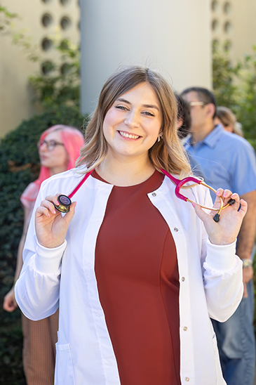 Portrait of graduate in her white coat holding her stethoscope.