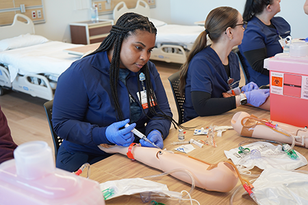 Students sitting around a table learning to insert IVs using mannequin arms.