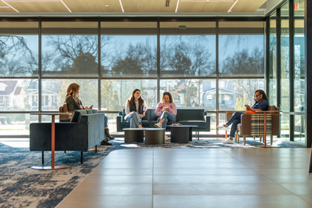 Students sitting on couches in the lounge area by the windows.