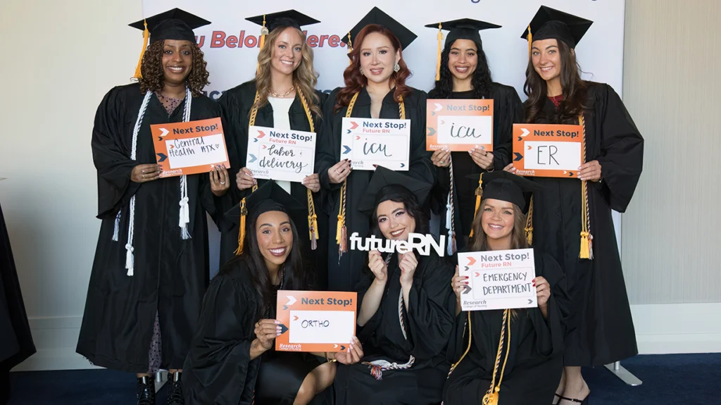 Portrait of students at graduation holding signs showing the places they will be working after graduation.