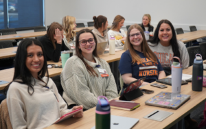 Portrait of four students in the classroom smiling at the camera.